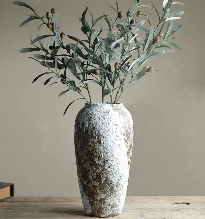 Decorative vase with greenery on a wooden surface against a plain background