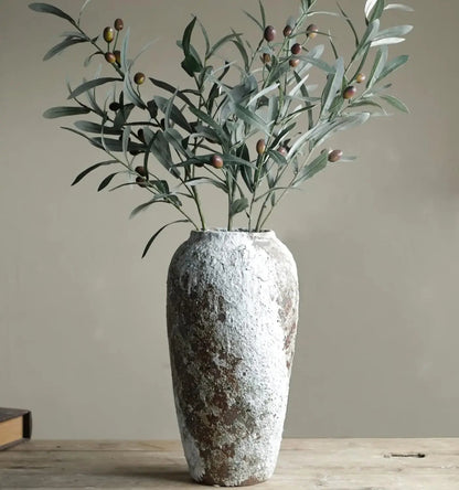 Decorative vase with greenery on a wooden surface against a plain background