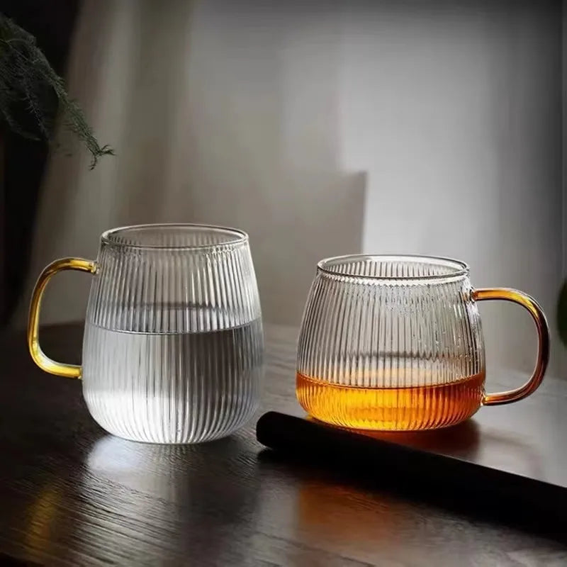 Two ribbed glass mugs with amber handles, one filled with clear water and the other with a dark-colored liquid.