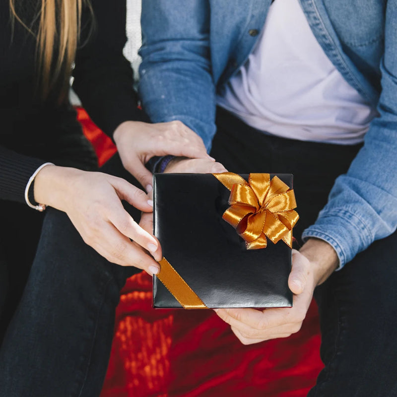 Two people holding a black gift box with a gold ribbon