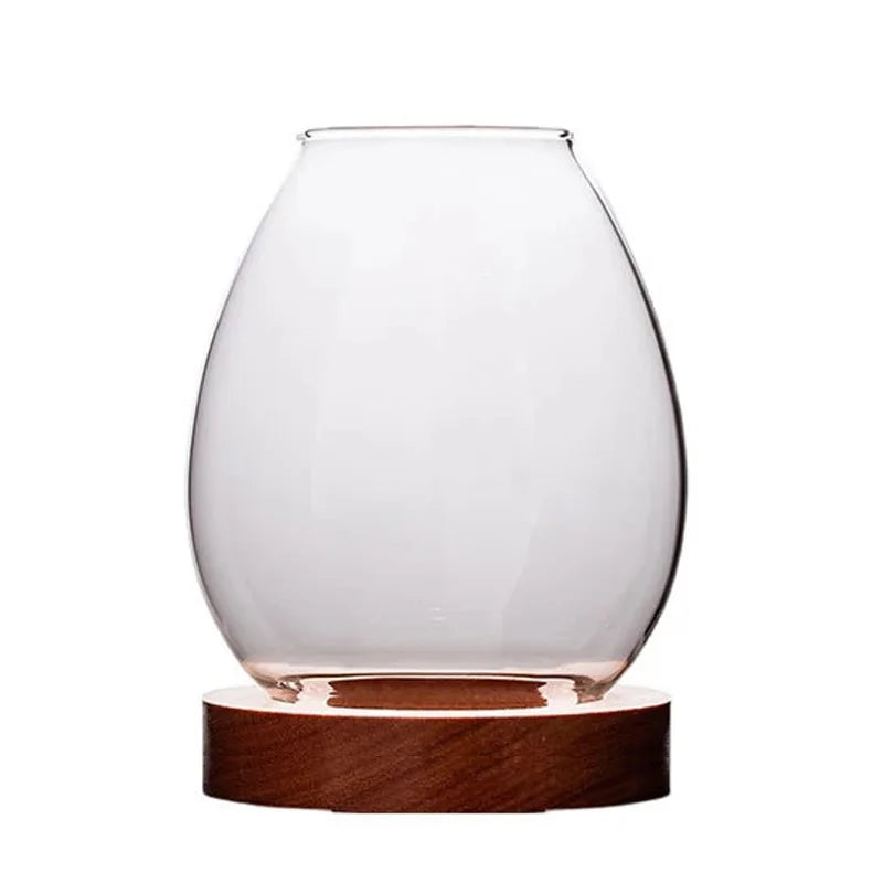 A minimalist glass candle holder with a wooden base, photographed against a plain white background. The transparent glass dome is designed to encase a tealight candle, enhancing the aesthetic of modern home decor.