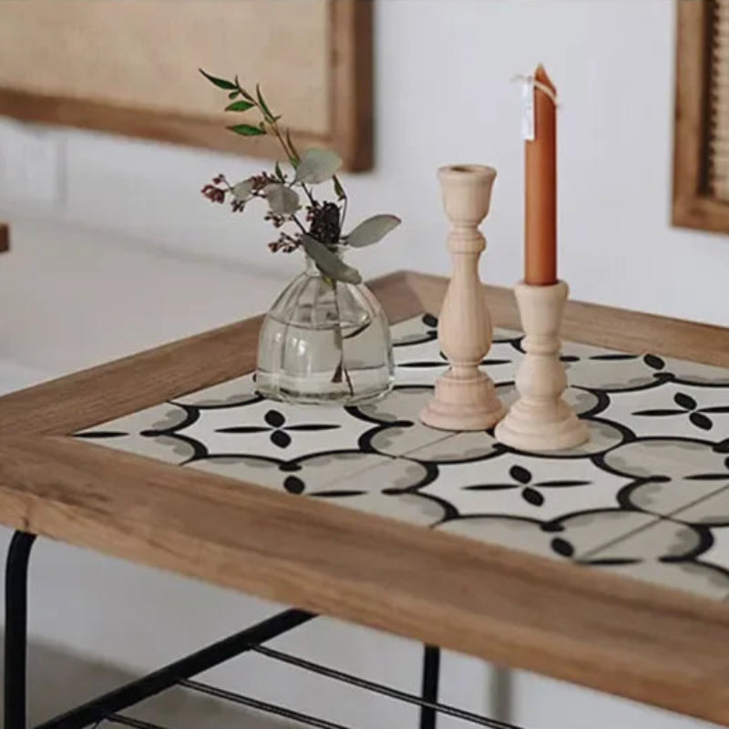 A glass vase with greenery and two wooden candle holders, one with a rust-colored candle, sit on a tiled side table.