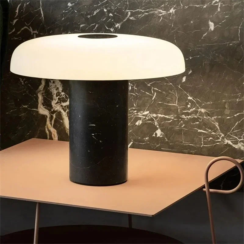 A modern mushroom-shaped table lamp with a dark marble base and a white dome shade, on a light pink table.