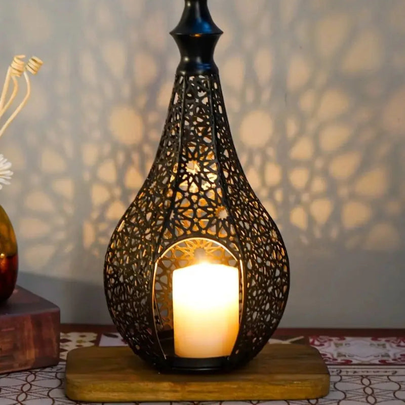 A close-up of a black ornate lantern with a lit candle, sitting on a wooden base and casting a patterned shadow on the wall behind it.