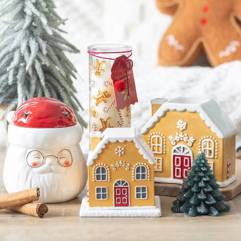 Decorative gingerbread house, candle, and Christmas tree on a table with a blurred background