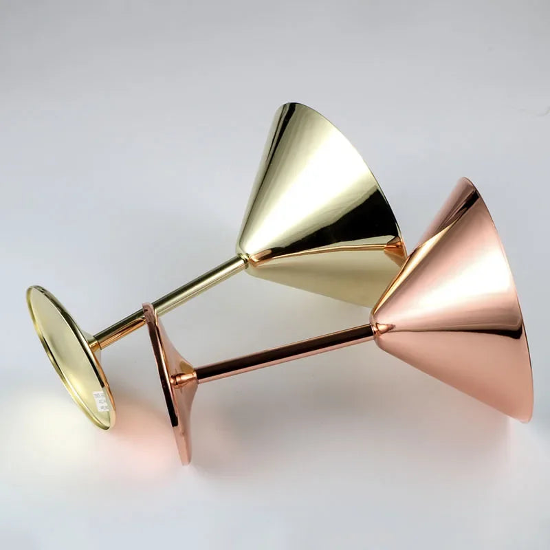 Two polished metal martini glasses, one gold and one copper, lying on a white surface.