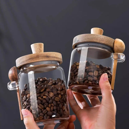 Two glass jars with wooden lids filled with coffee beans held by a hand against a dark background