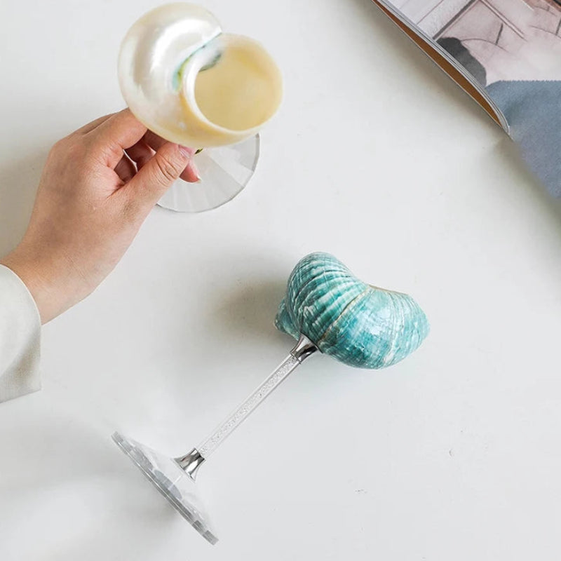 Hand holding a glass with a blue and white marbled soap bar, placed on a white surface.