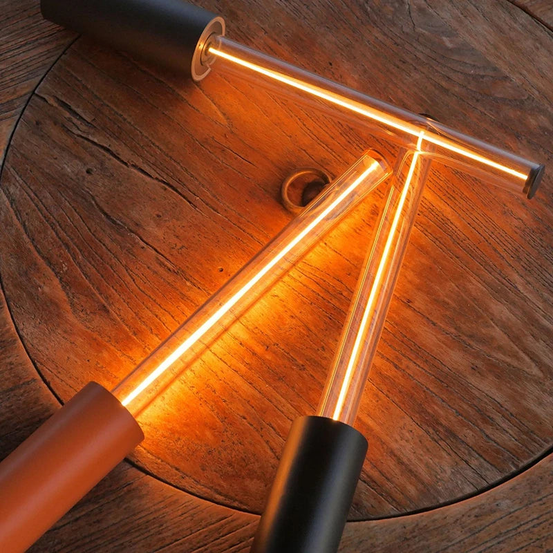 A close-up shot of three long, cylindrical lamps with glowing tubes, two black and one red, arranged in a triangular shape on a wooden table.