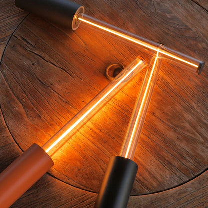 A close-up shot of three long, cylindrical lamps with glowing tubes, two black and one red, arranged in a triangular shape on a wooden table.