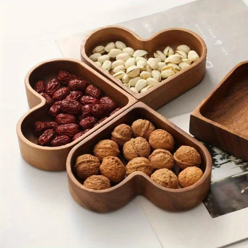 Three heart-shaped wooden bowls filled with pistachios, walnuts, and dried dates, with a partial view of a fourth empty bowl.