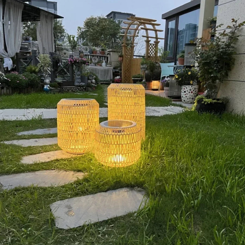 Two illuminated outdoor lanterns on a grassy area with a modern house in the background.