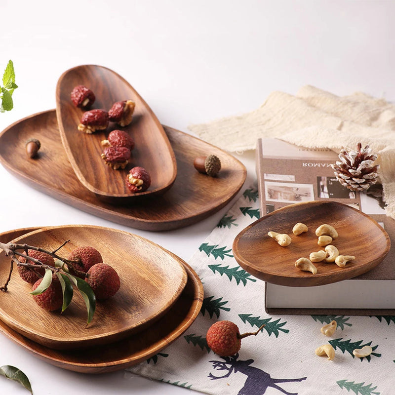 Wooden serving dishes holding lychees, red dates, and cashews, arranged on a table with a holiday-themed cloth, an acorn, and a pine cone.