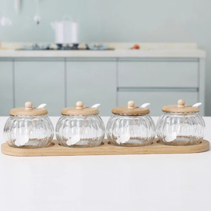 Four empty pumpkin-shaped glass jars with wooden lids and spoons, on a bamboo tray.
