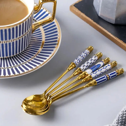Set of gold spoons with blue and white patterns next to a blue and white striped teacup and saucer.