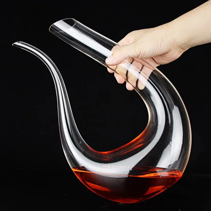 A hand holding a swan-shaped glass wine decanter filled with red wine.