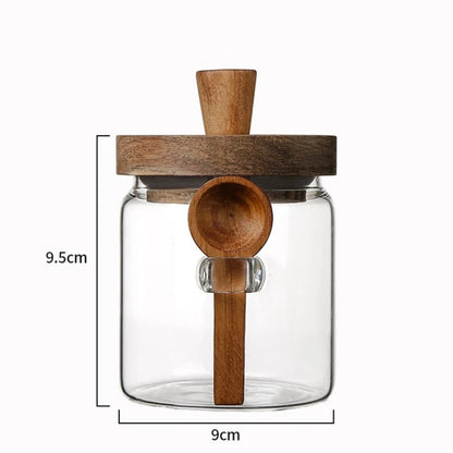 Clear glass jar with wooden lid and spoon, featuring dimensions on a white background.