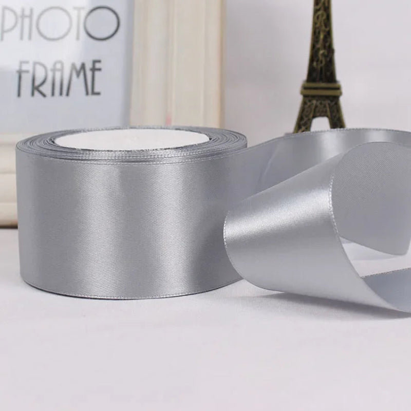 Silver satin ribbon with a spool on a light gray surface.