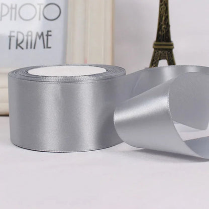 Silver satin ribbon with a spool on a light gray surface.