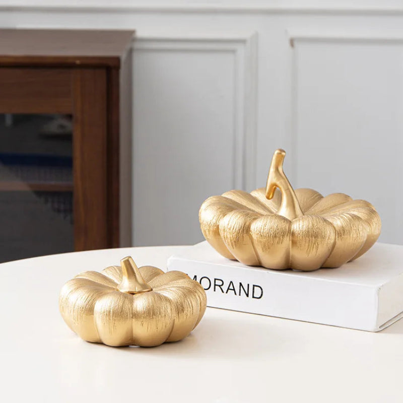 A textured gold decorative pumpkin with a small stem sits in front of a larger textured gold pumpkin on a book.