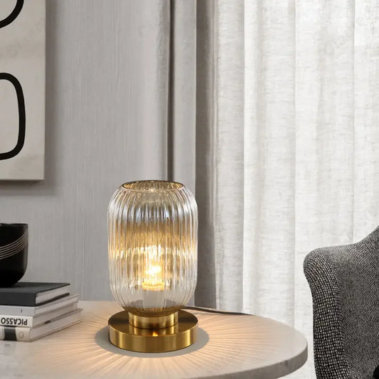 Lit amber glass lamp with a gold base on a round table next to books and a chair.