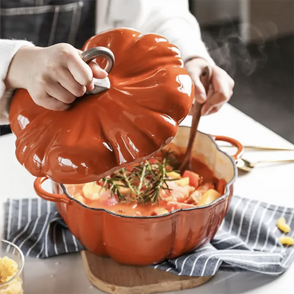 A person lifts the pumpkin-shaped lid off an orange cast iron pot filled with a steaming stew.
