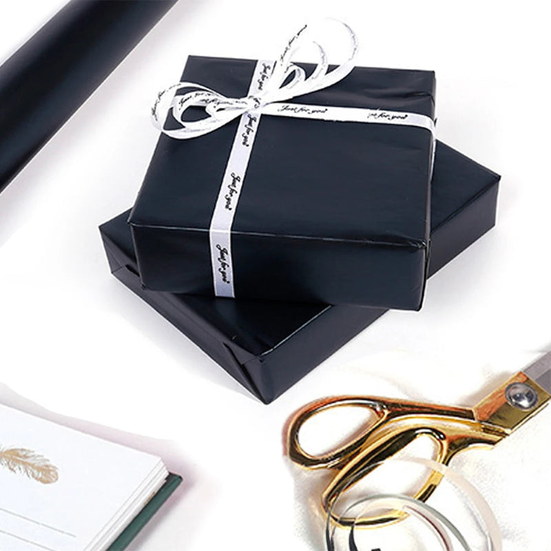 Black gift box with a white ribbon, gold scissors, and a white notebook on a white background