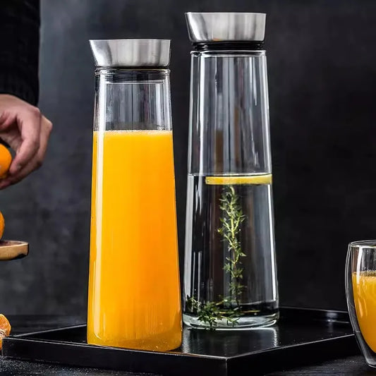 Two glass carafes with metal lids, one filled with orange juice and the other with water and a lemon slice.