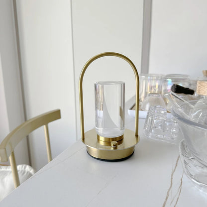 A portable table lamp with a gold metal frame and a glass shade, placed on a white marble table.