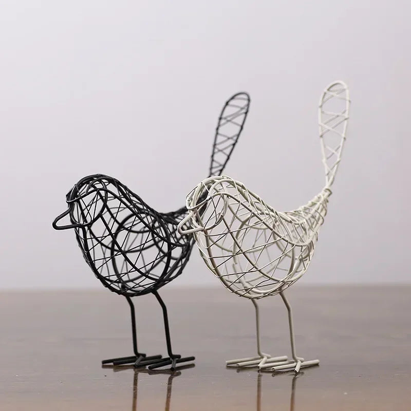 Two wire bird sculptures, one black and one silver, on a reflective surface with a neutral background.