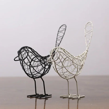 Two wire bird sculptures, one black and one silver, on a reflective surface with a neutral background.