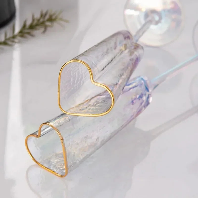 Two heart-shaped champagne flutes with gold rims lying on a marble surface.