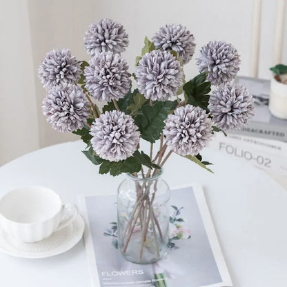 Light purple faux flowers in a clear vase on a white table.