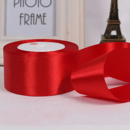 Red satin ribbon with a spool on a light surface, Eiffel Tower model in the background.