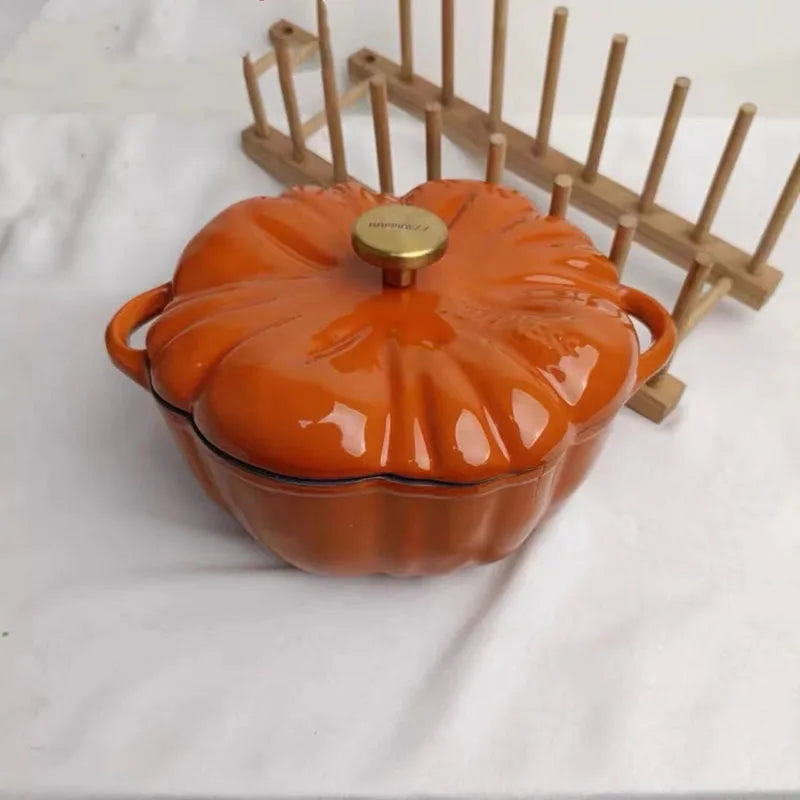 An orange, pumpkin-shaped cast iron pot with a gold knob sits next to a wooden dish drying rack.
