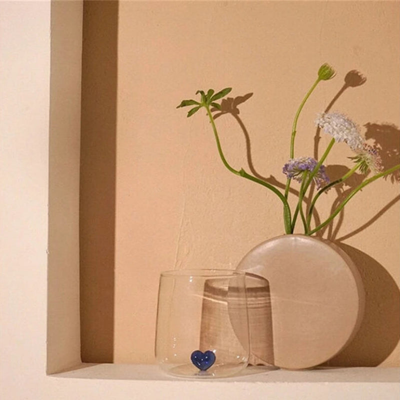A glass with a blue heart and a vase of flowers.
