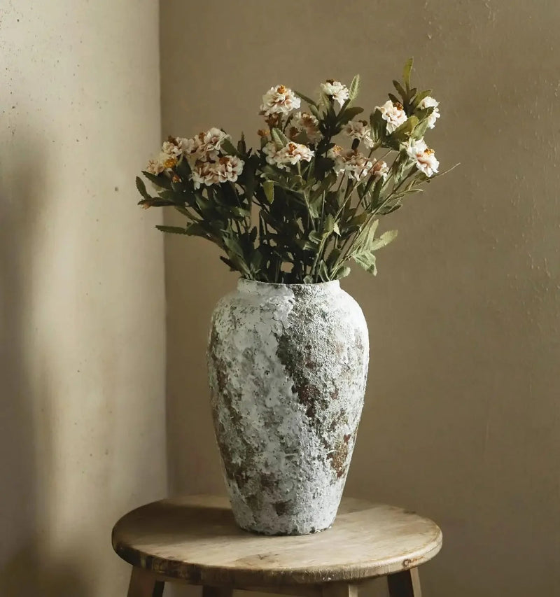 Decorative vase with flowers on a wooden stool against a beige wall