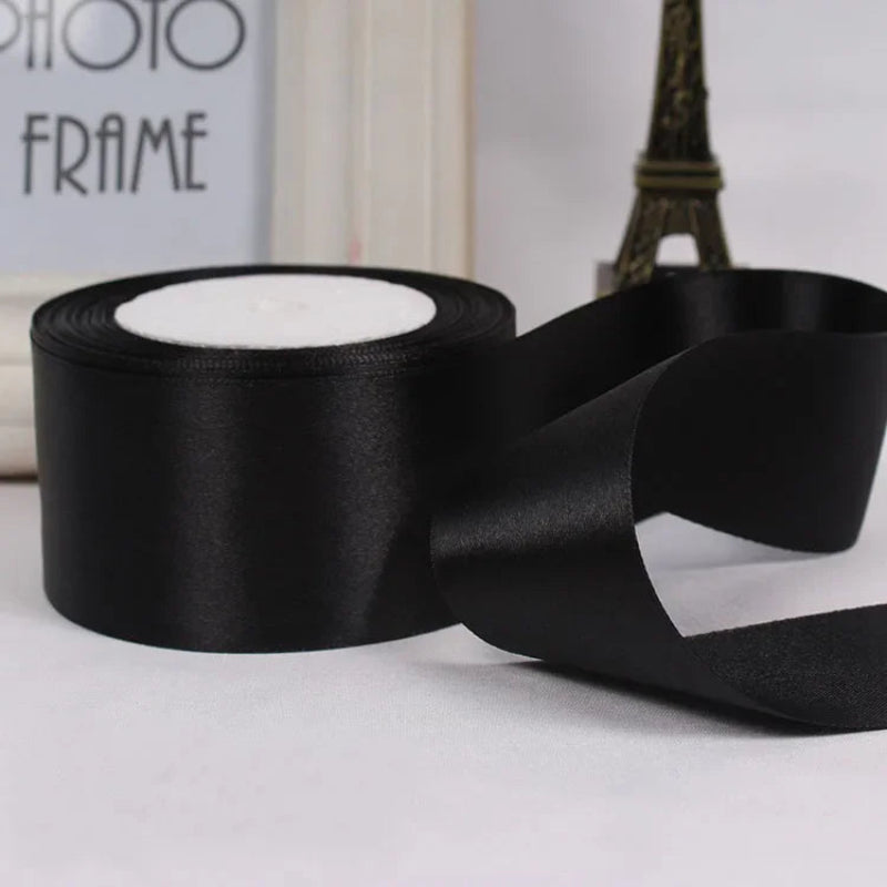 Black satin ribbon with a roll and a swatch on a light surface.