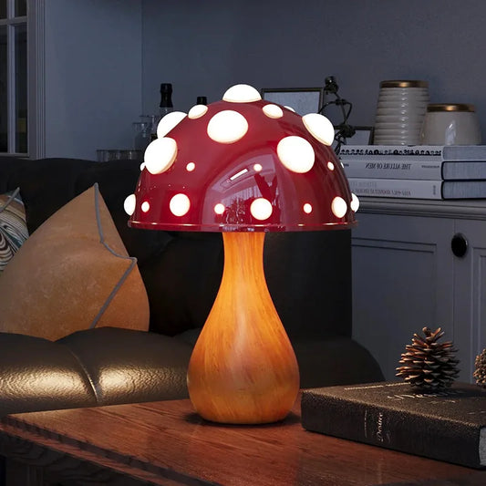 A mushroom-shaped lamp with a red spotted cap and a wooden stem, illuminating a dark room with a book and pinecone on a table.