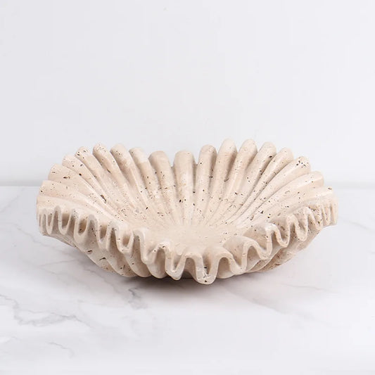 Scalloped travertine bowl on a coffee table styled with decorative accents.