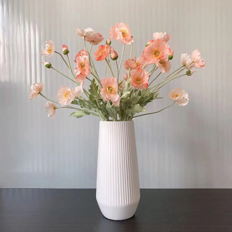 A white ribbed vase holds a bouquet of pink and orange poppies.