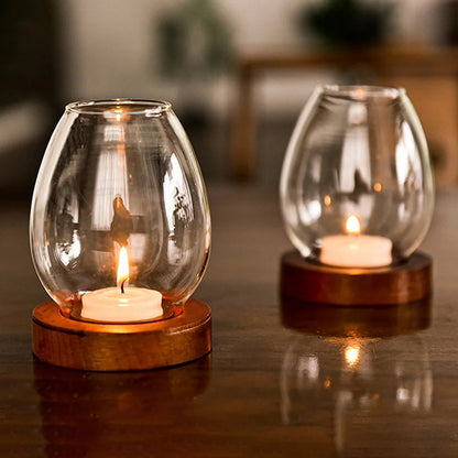 Two glass candle holders with wooden bases, each containing a lit tea light candle, placed on a reflective wooden surface. The warm candlelight enhances the cozy and elegant ambiance of the room.