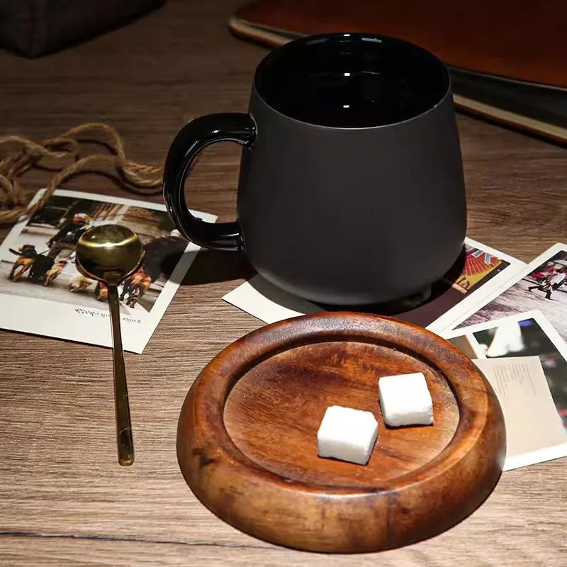 A black mug and a wooden coaster with two sugar cubes and a gold spoon on a wooden table with old photographs.