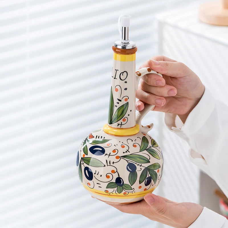Decorative ceramic oil bottle with artistic design held by a person against a white background