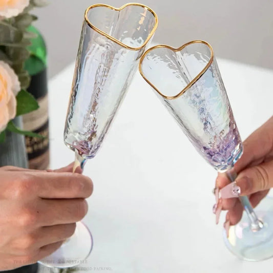 Two heart-shaped champagne flutes clinking together, held by two people.