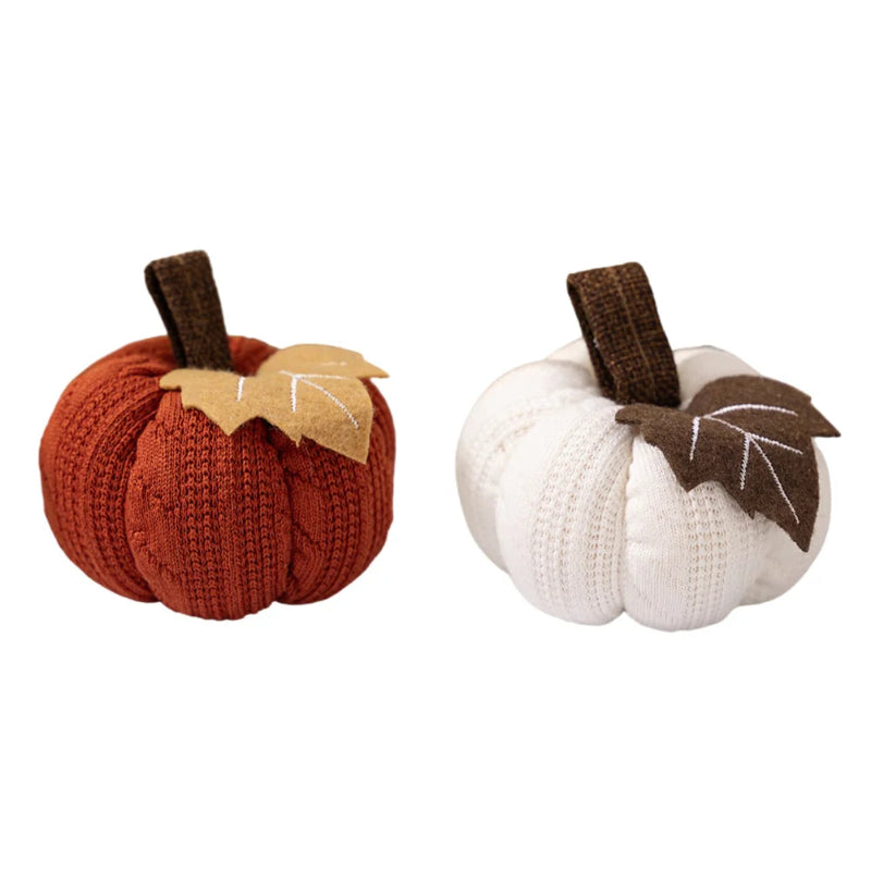 Two knitted pumpkins, one orange and one white, each with a brown stem and a fabric leaf, isolated on a white background.