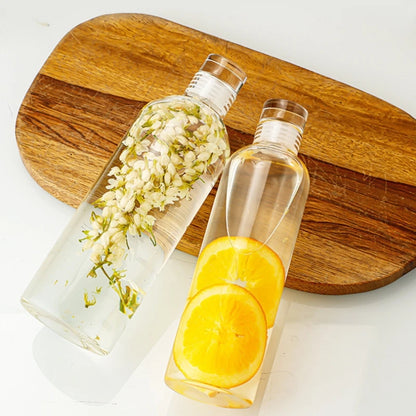 Two clear bottles on a wooden board, one with flowers, one with orange slices.