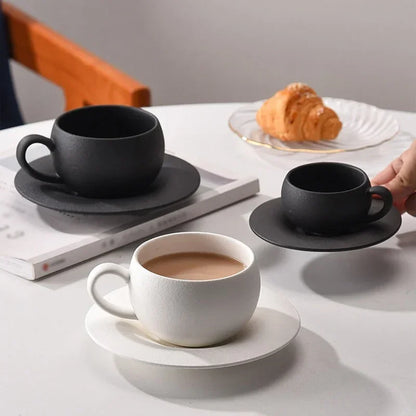 Three textured coffee cups and saucers, two black and one white, with a croissant.