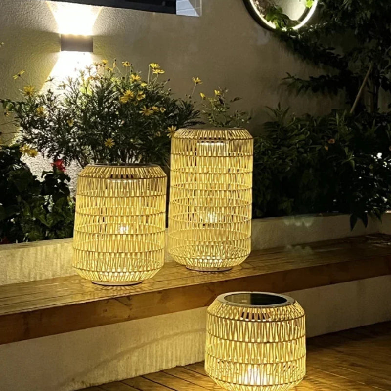 Three woven lanterns on a wooden surface with plants and a wall light in the background