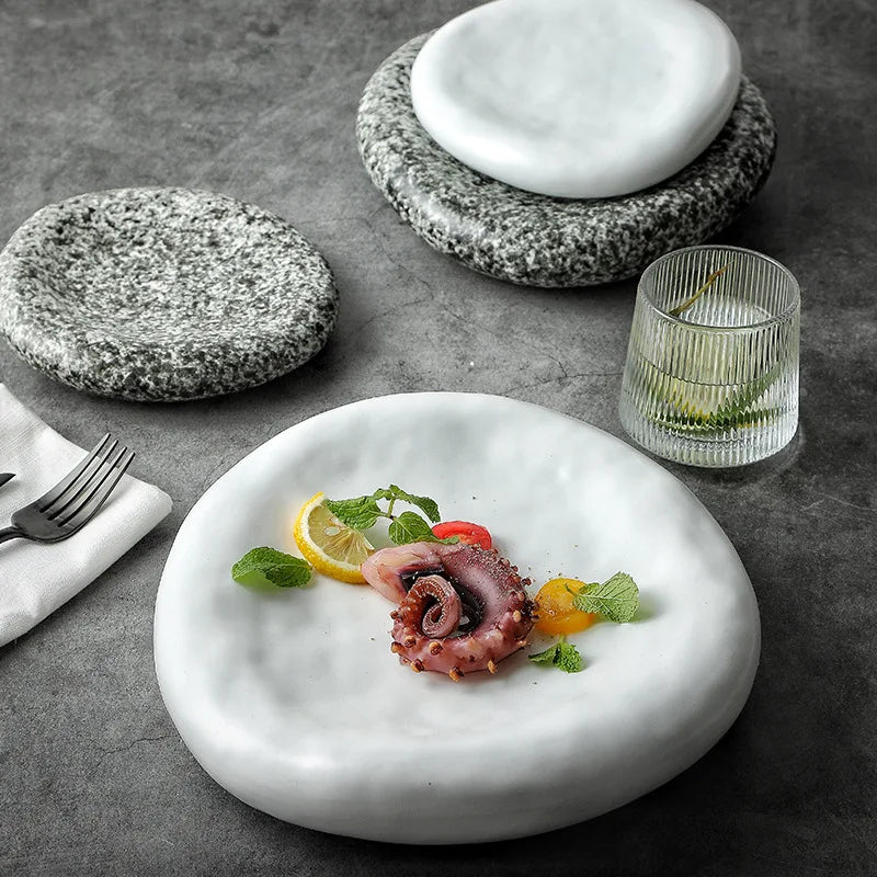 Marble-like stone plates with a dish of octopus and vegetables on a gray surface.